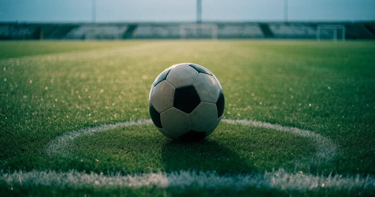Uma bola de futebol no ponto central de um relvado, à luz da manhã